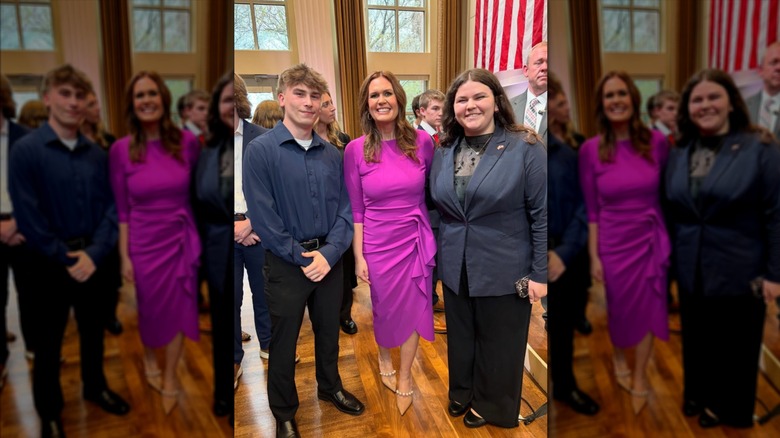 Sarah Huckabee Sanders dans une robe magenta et des talons nus posant avec deux personnes
