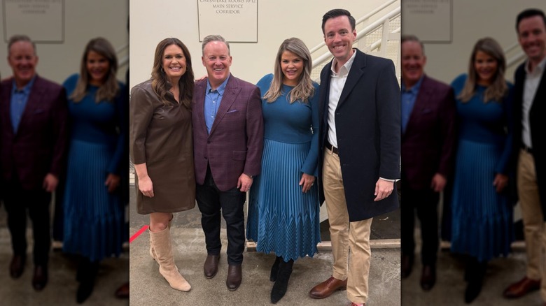 Sarah Huckabee Sanders portant une robe droite marron et des bottes en daim jusqu'aux genoux en posant avec trois autres personnes