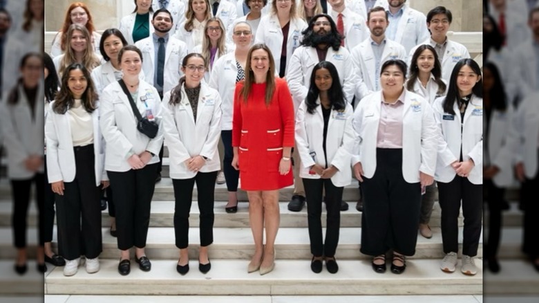 Sarah Huckabee Sanders dans une robe rouge et entourée d'étudiants en médecine en blouse blanche sur des marches en marbre