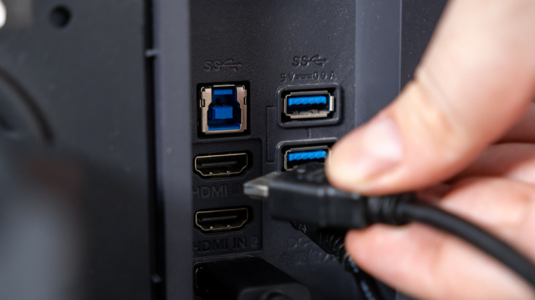 Gros plan de la main d'une personne branchant un câble HDMI noir sur le port HDMI IN 2