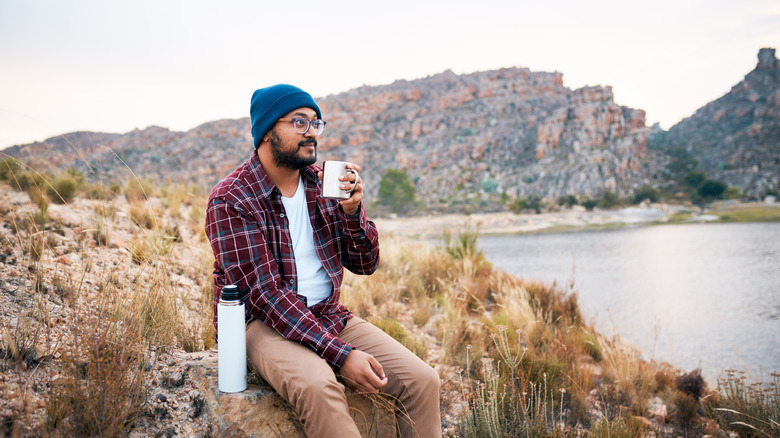 un homme boit du café au bord d'un lac