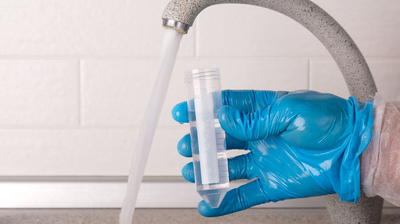 La main dans un gant bleu aspire l'eau d'un robinet de cuisine dans un tube à essai.
