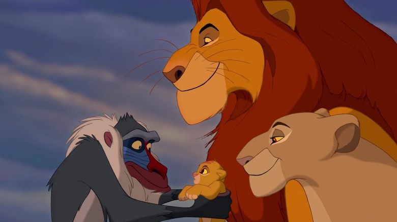 Rafiki tient Simba dans ses bras pendant que ses parents le regardent dans Le Roi Lion