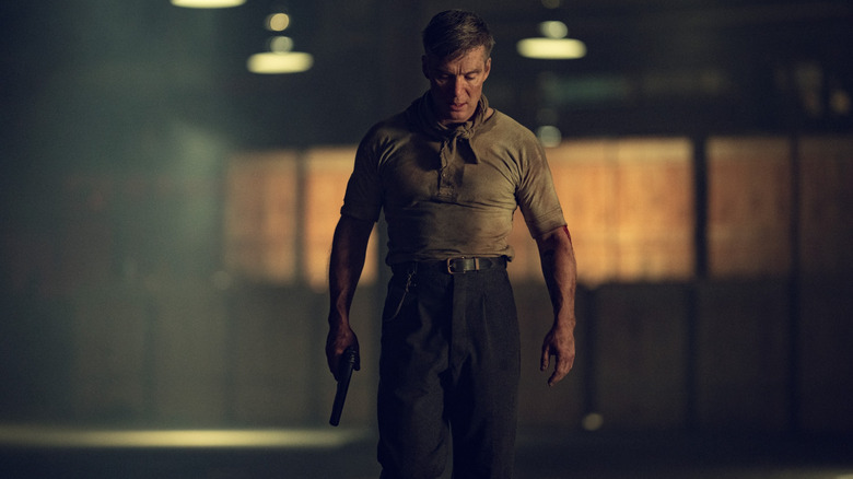 Cillian Murphy dans le rôle de Tommy Shelby couvert de terre et tenant une arme à la main alors qu'il traverse un entrepôt vide dans Peaky Blinders : The Immortal Man