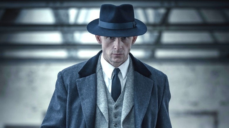 Duke Shelby portant un pardessus sombre et un chapeau dans la série suite de Peaky Blinders