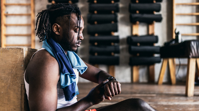 Homme assis dans une salle de sport tout en vérifiant sa montre intelligente