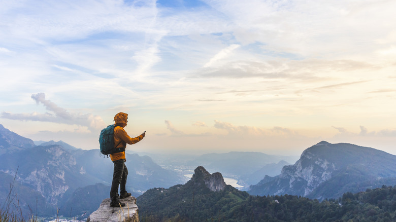 Un randonneur au sommet d’une montagne regarde son téléphone.