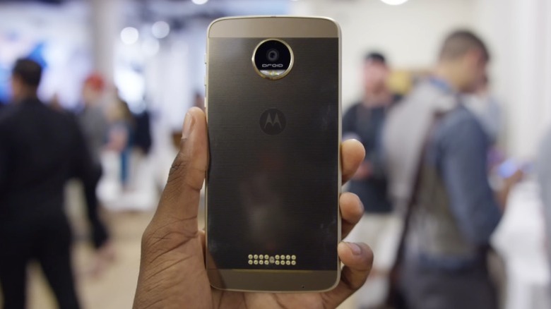 Main tenant un Moto Z avec des personnes floues en arrière-plan