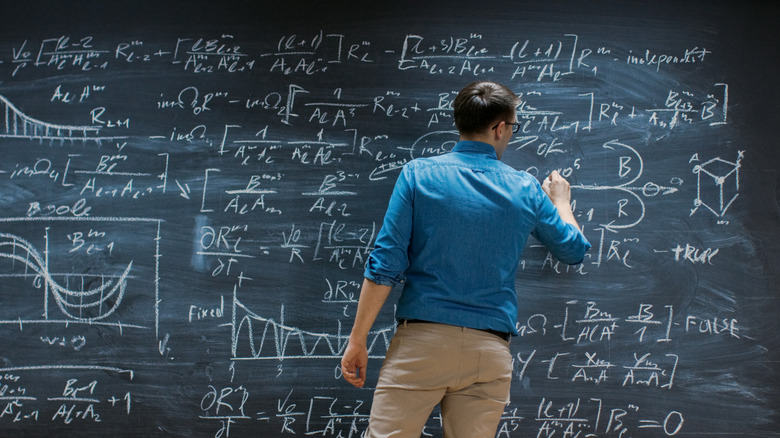 Mathématicien debout devant un tableau rempli d'équations physiques