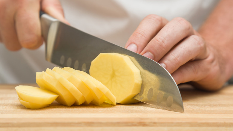Chef coupant la pomme de terre en fines tranches