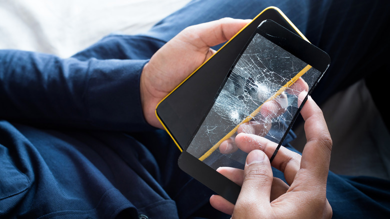 Un homme tenant un smartphone et un verre trempé endommagé