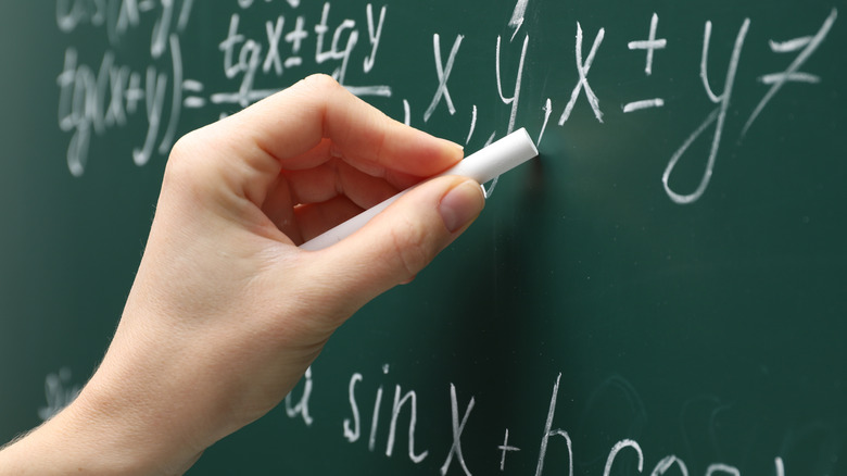 Un gros plan d'une main écrivant des équations mathématiques sur un tableau.