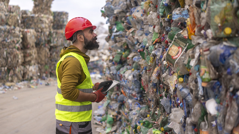 Un employé du dépôt de déchets examine une grande masse de déchets plastiques