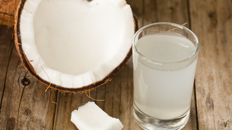 Un verre d'eau de coco sur la table à côté d'un fruit de noix de coco coupé en deux