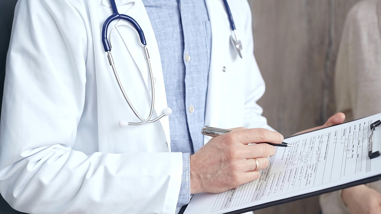 Un médecin tenant un presse-papiers et prenant des notes.