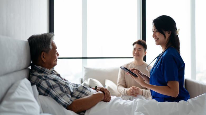 Un professionnel de la santé est assis sur un lit et parle à un homme âgé qui est assis dans le lit.