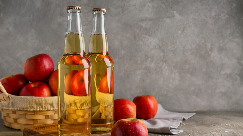 Bouteilles fraîches de cidre de pomme et de pommes dans un panier en osier