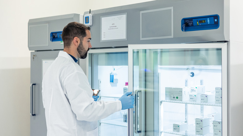 Scientifique en blouse et gants ouvrant un réfrigérateur dans un laboratoire