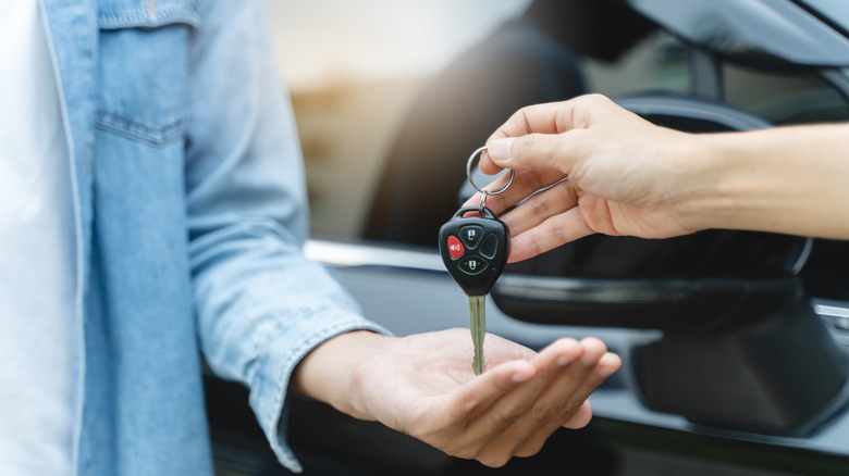 Gros plan d'une main plaçant les clés de voiture dans la paume de quelqu'un d'autre avec un véhicule noir en arrière-plan