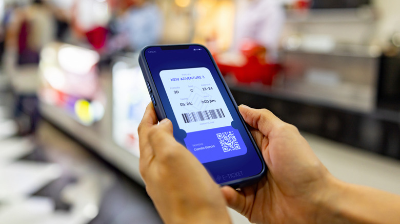 Gros plan d'un billet de cinéma affiché sur un téléphone intelligent dans les mains de quelqu'un près du stand de concession d'une salle de cinéma