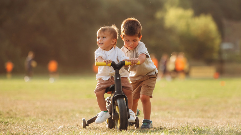 deux enfants jouent dans un champ herbeux sur un vélo en plastique
