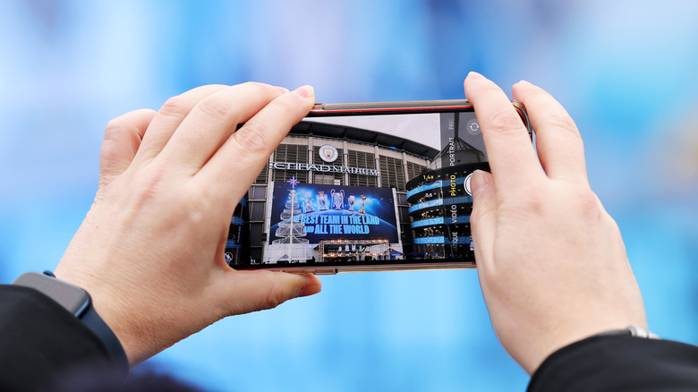 Mains tenant un iPhone prenant une photo du stade Etihad