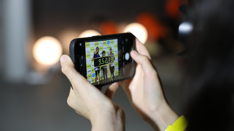 Mains tenant un iPhone prenant une photo de trois marathoniens