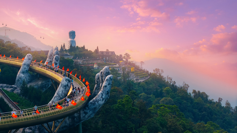 Pont soutenu par des mains en pierre dans les collines de ba na contre un ciel rose au coucher du soleil.