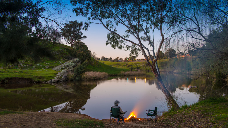 un homme est assis devant un feu de camp à côté d'un billabong en Australie