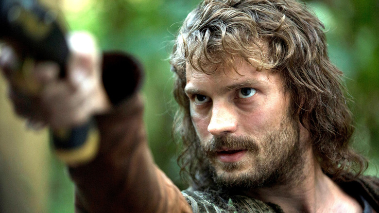 Jamie Dornan dans le rôle d'Abe Goffe avec des cheveux longs et une barbe et levant le bras dans une forêt dans New Worlds