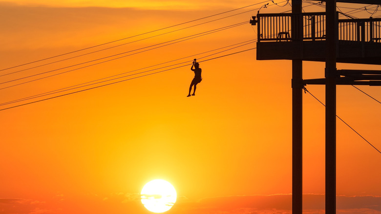 Silhouette d'une personne sur la tyrolienne à WildPlay Element Parks Jones Beach pendant le coucher du soleil