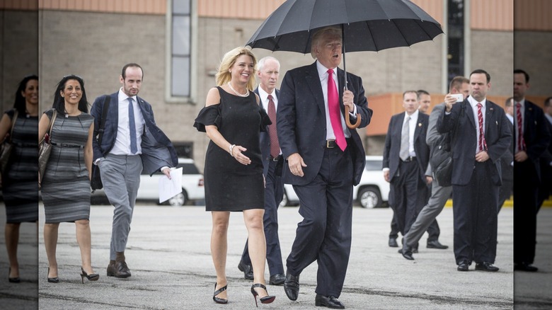 Pam Bondi sort à côté de Donald Trump qui tient un parapluie au-dessus de lui