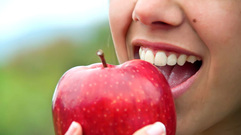Photo d'une femme avec la bouche ouverte, s'apprêtant à croquer dans une pomme.