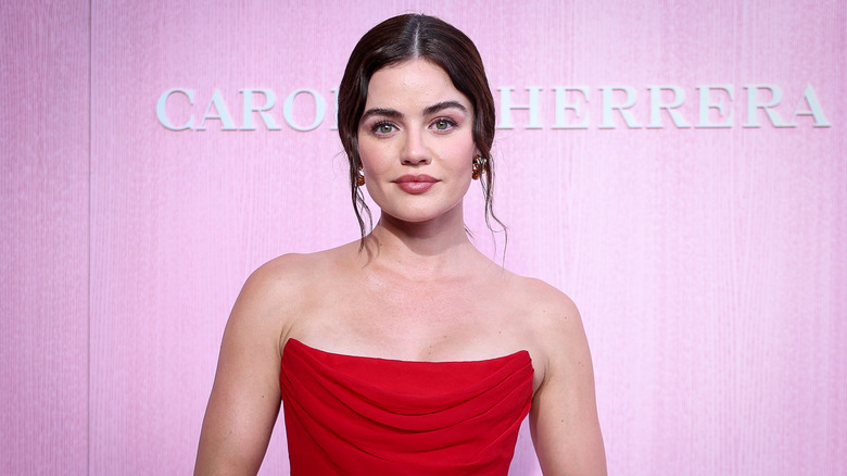 Lucy Hale porte une robe bustier rouge en posant devant un fond rose