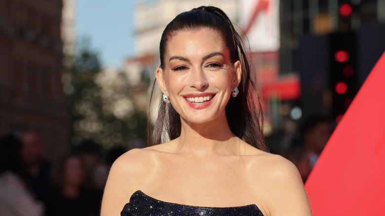 Anne Hathaway sourit sur une photo ensoleillée prise lors d'un événement sur le tapis rouge en plein air