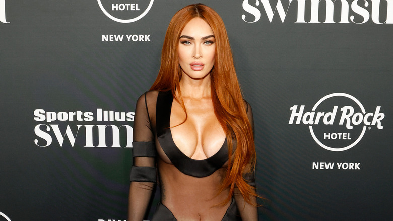 Megan Fox porte une robe noire transparente et plongeante et a les cheveux roux séparés au milieu