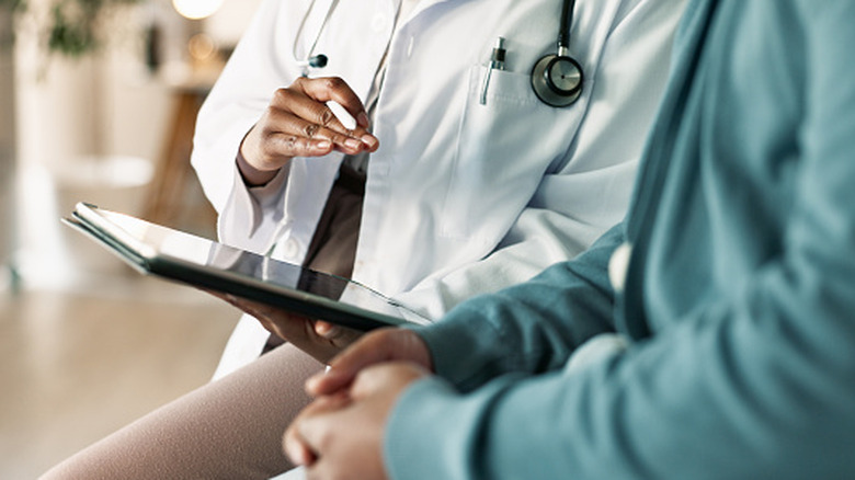 Un médecin tenant une tablette parlant à un patient.