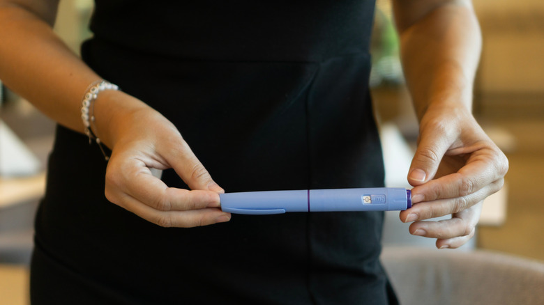 Gros plan d’une personne vêtue d’une robe noire tenant un stylo injecteur Ozempic.