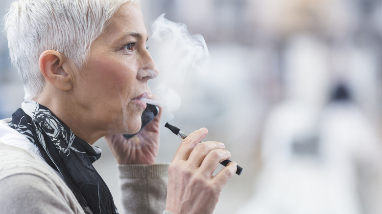 Femme âgée aux cheveux gris vapotant une e-cigarette au téléphone