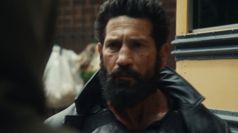Jon Bernthal dans le rôle de Frank Castle passant devant un bus scolaire portant sa tenue Punisher dans The Punisher : One Last Kill