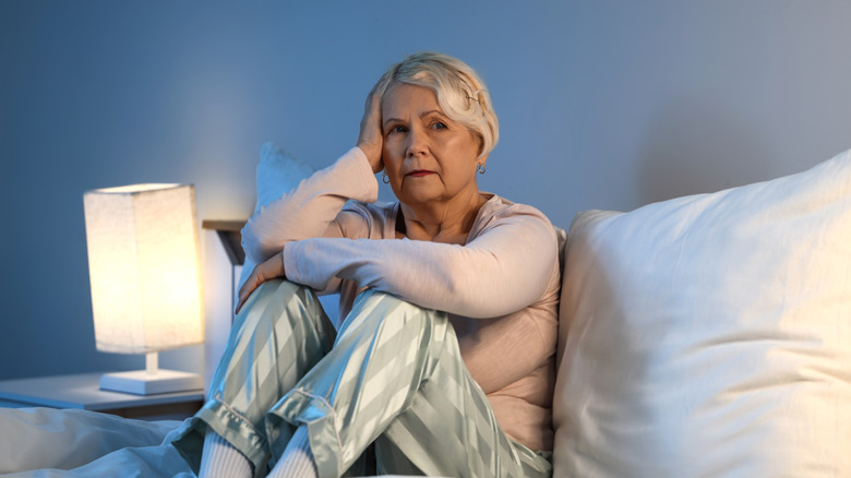 Femme plus âgée assise dans son lit en pyjama, l'air inquiet sur son visage