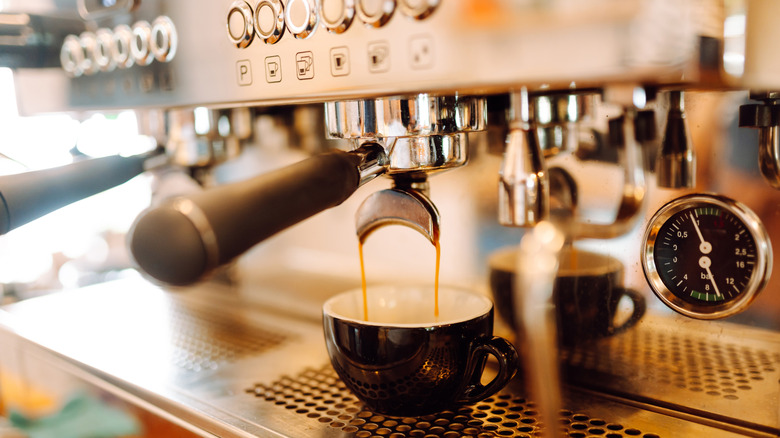 Espresso versé d'une machine à expresso dans une tasse de couleur foncée. Un cadran de pression sur la machine indique une pression d'environ 10 bars.