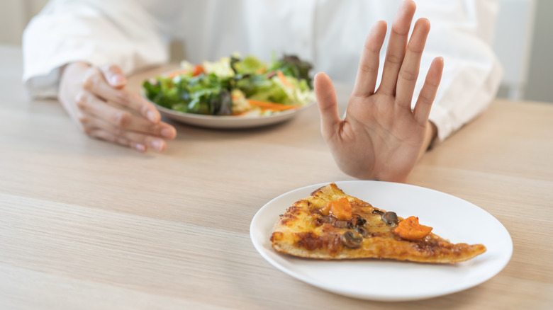 Main repoussant une tranche de pizza en faveur de la salade