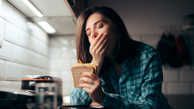 Femme tenant un sandwich en bâillant dans la cuisine