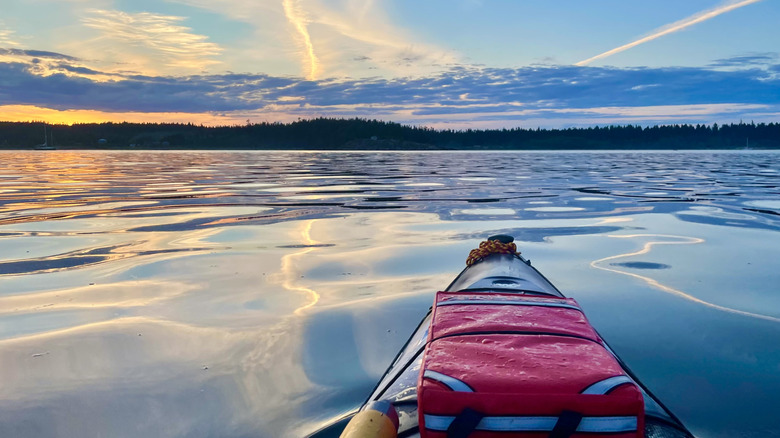 Kayak sur l'eau avec de belles couleurs et nuages ​​de coucher de soleil de ciel orange et bleu