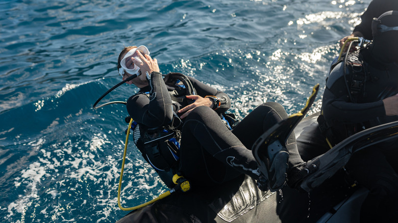 Un plongeur en tenue de plongée roule à reculons hors du bateau dans l'eau