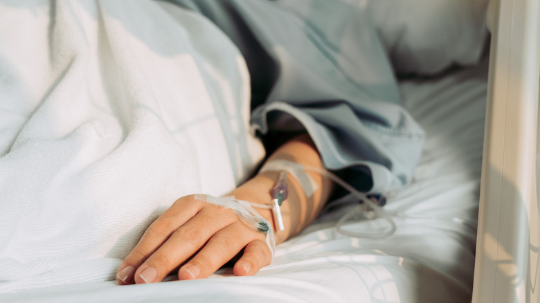Bras et main d'une femme allongée dans un lit d'hôpital avec un tube IV connecté à sa main