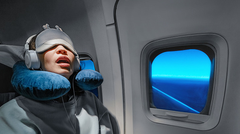 Femme au siège de la fenêtre de l'avion avec masque pour les yeux et oreiller cervical