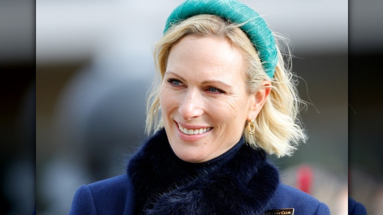Zara Tindall sourit lors d'un événement, portant un grand bandeau vert