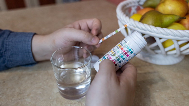 Un homme teste la qualité de l’eau dans une cuisine à l’aide de bandelettes de test